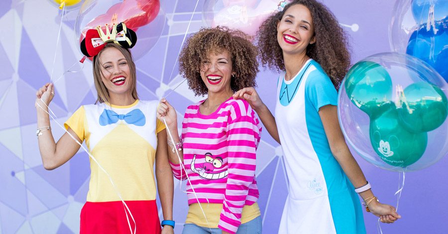 Three friends pose with balloons in front of the purple wall at Magic Kingdom Park